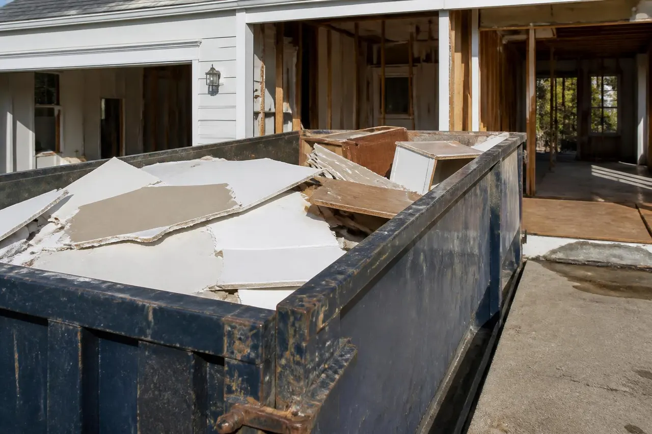 Torn-out drywall, framing lumber, and flooring piled inside a demolition dumpster